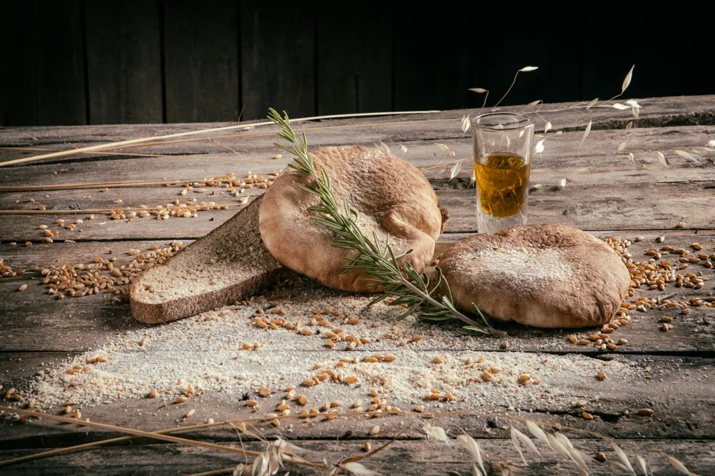 Pane tradizionale delle Madonie con spighe di grano, rosmarino e un bicchiere d'olio d'oliva su un tavolo di legno, dal progetto Pane Nostro